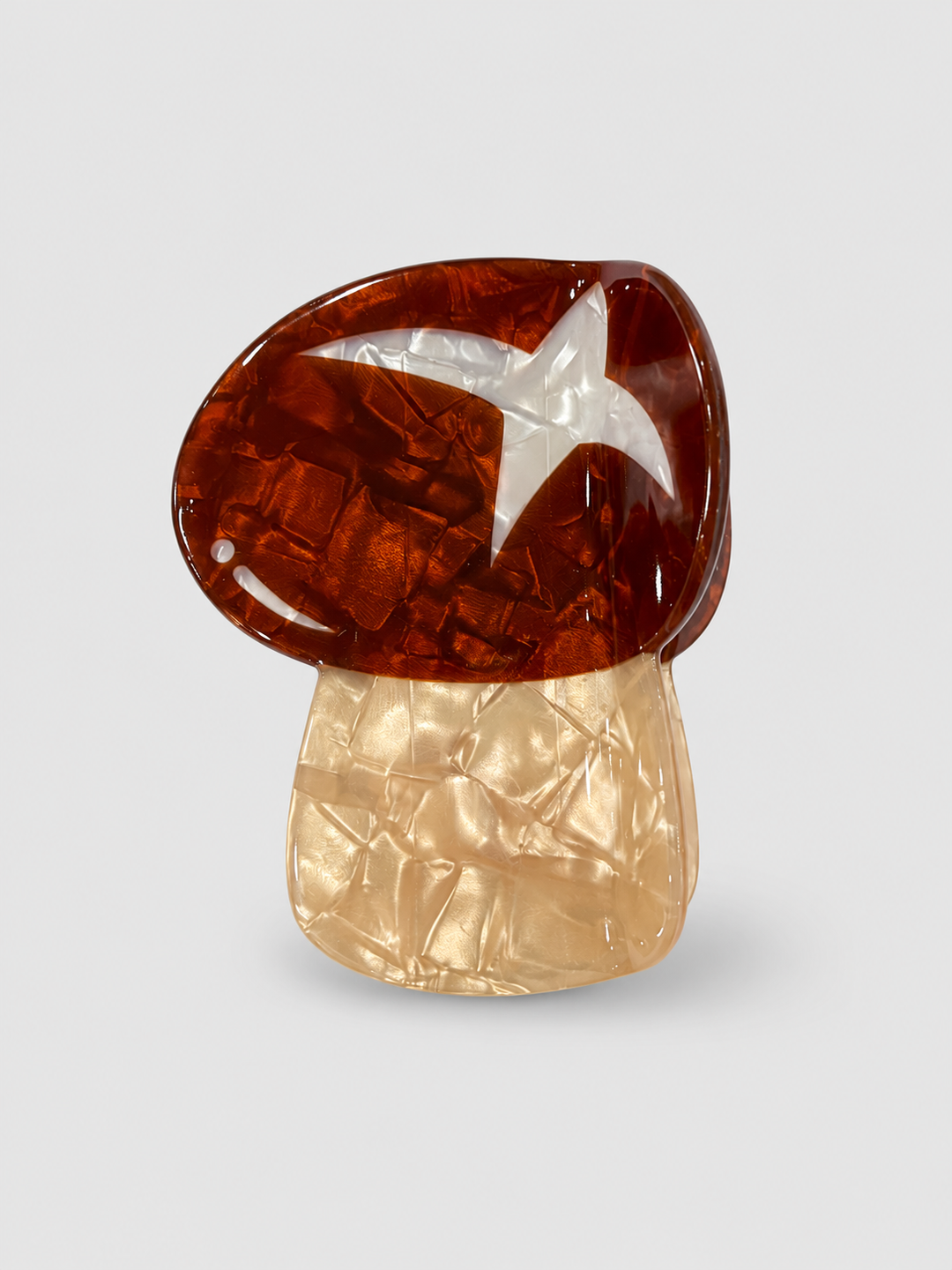 Amber and champagne pearlescent mushroom hair claw clip with a white star on a pale grey background.