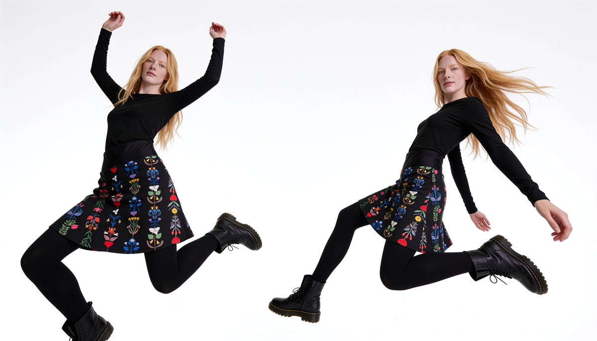 A model with long red hair, in a black top, black tights and boots, jumps in a folk-floral Katrin Leblond Art Skirt.